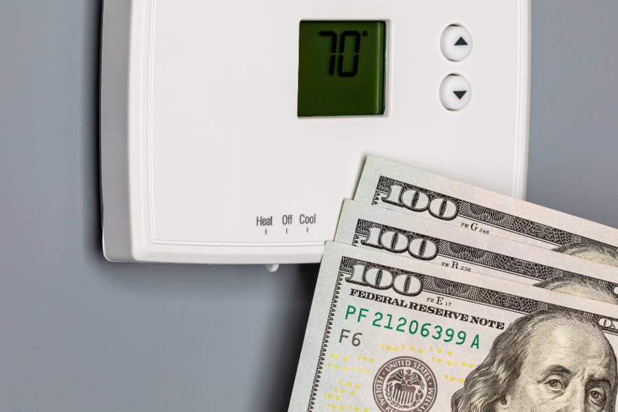 Hundred dollar bills in front of a thermostat.